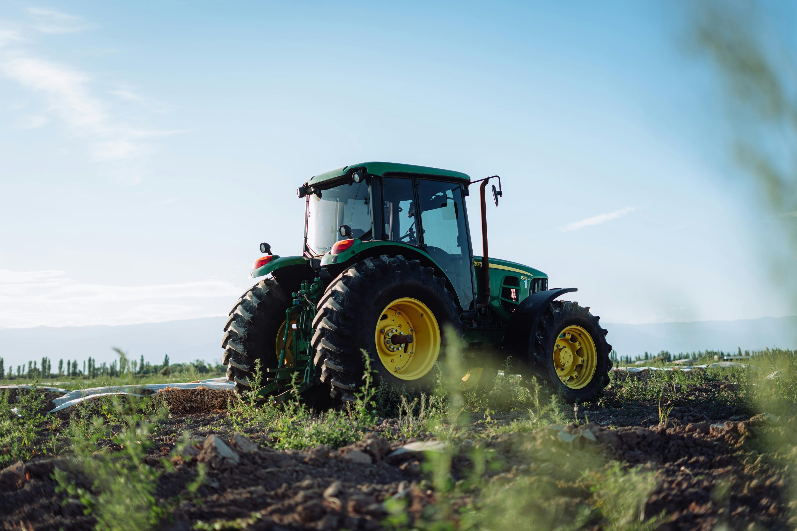 A vibrant green tractor on a farm in Mendoza, Argentina, under clear blue skies.